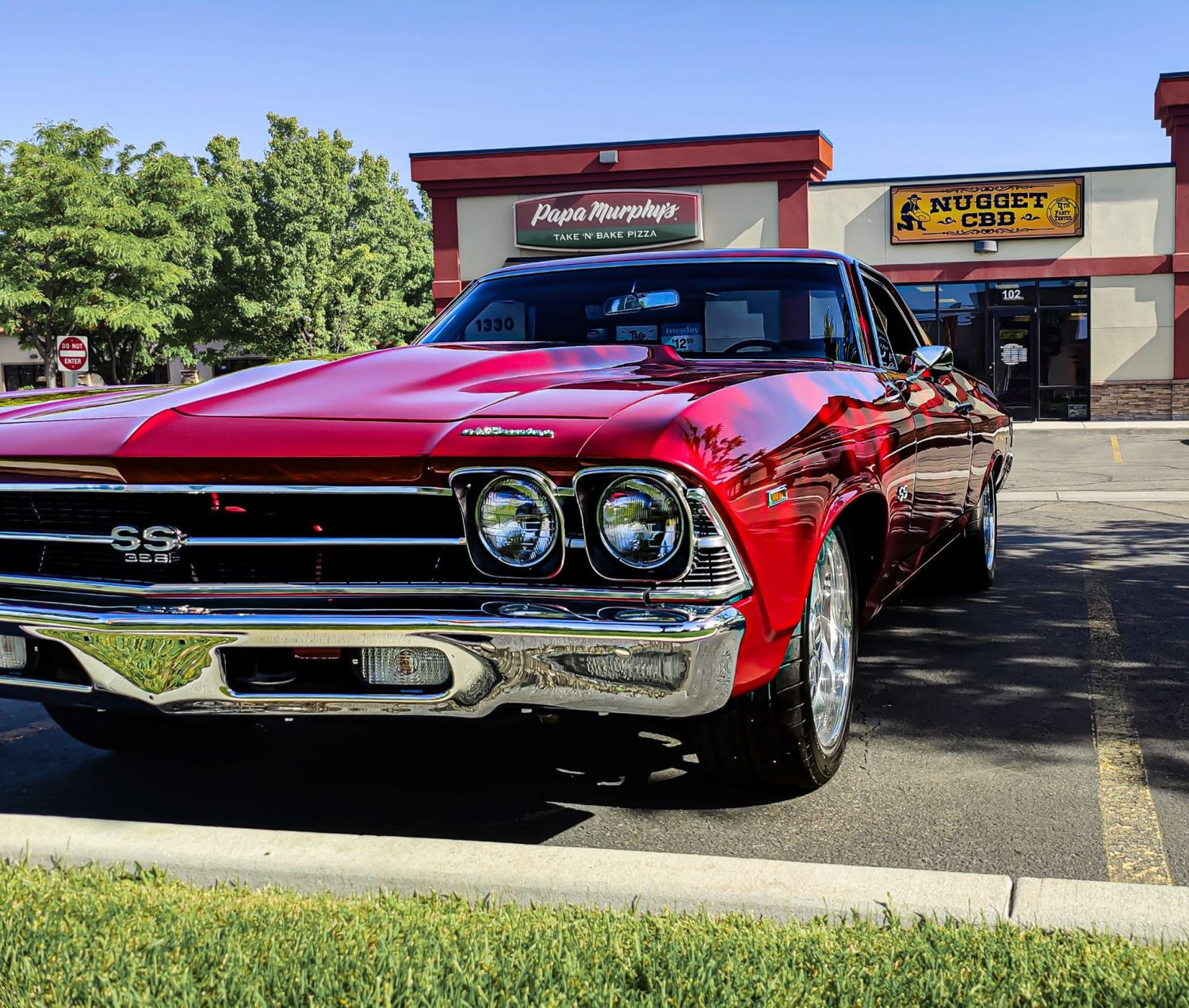 Red classic car parked in front of a building with 'Papa Murphy's' and 'Nugget & Cbd' signs.
